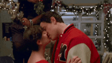a man wearing a red varsity jacket with the letter r on it kisses a woman
