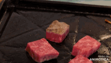 a few pieces of meat are cooking on a black surface with the words made in animotica on the bottom