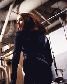 a woman in a black jacket stands in a dark room