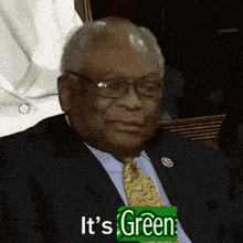 a man in a suit and tie with a green sign that says it 's green on it