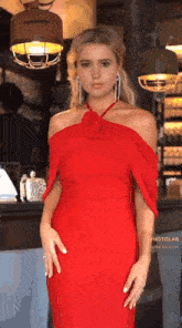 a woman in a red off the shoulder dress is standing in front of a counter .