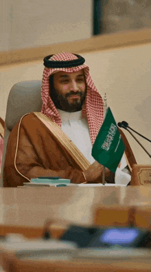 a man sitting at a table holding a small green flag with arabic writing on it
