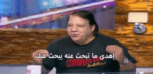 a man in a black shirt is sitting at a table with a cup of coffee and talking in arabic .