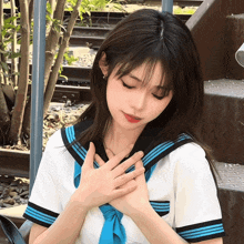 a girl in a school uniform with a blue tie holds her hands on her chest
