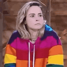 a woman wearing a rainbow colored sweatshirt is looking at the camera .