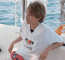 a young man is sitting on a boat in the water wearing a white shirt .