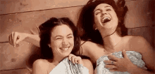 two naked women are laughing while wrapped in a towel .
