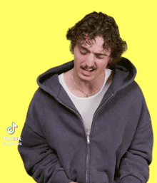 a man wearing a grey hoodie and a white shirt has a tiktok sticker on his face