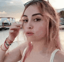 a woman wearing a white tank top and bracelets on her wrists looks at the camera