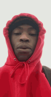 a man wearing a red hoodie and a black hat looks at the camera