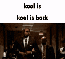 a man in a suit and tie is walking down a hallway with the words kool is kool is back below him
