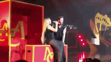 a woman is sitting on a box singing into a microphone while a man stands behind her