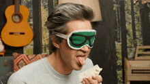 a man wearing a green goggles sticks his tongue out while eating a piece of bread