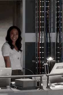 a woman is smiling while standing in front of a desk with a laptop .
