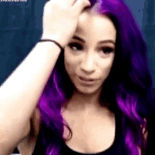 a woman with purple hair is holding her hand to her face .