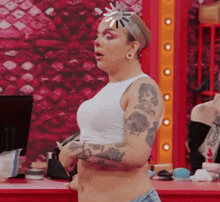 a woman with tattoos on her arms is wearing a white crop top and shorts .