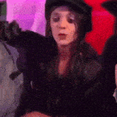 a woman wearing a hat and a leather jacket is sitting in front of a red and purple wall .