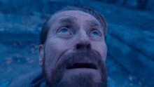 a man with a beard is looking up at the sky in a dark room .