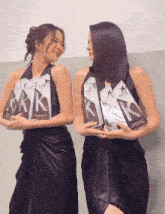 two women in black dresses are holding a stack of awards that say kaz