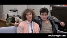 a man and a woman are sitting on a couch . the man is wearing a leather jacket .