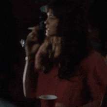 a woman in a red shirt holds a red cup in her hand