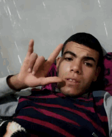 a young man in a striped shirt is making a peace sign with his fingers