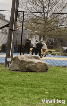 a group of people are playing basketball in a park with a large rock in the foreground .