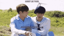 two young men are sitting next to each other in a field and hugging each other .