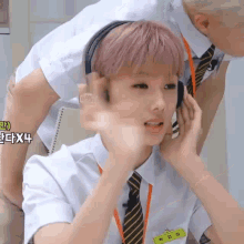 a boy with pink hair is wearing headphones and a tie while a man stands behind him .