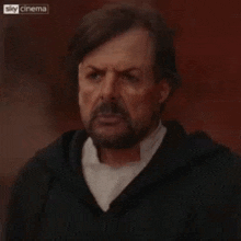 a man with a beard is making a funny face while holding his hands together .