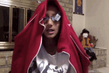 a woman wearing glasses and a red hooded sweatshirt has a card taped to her eye ..