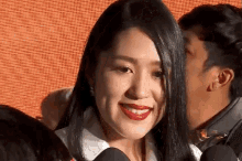 a woman with red lipstick smiles while a man whispers in her ear