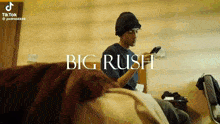 a man sitting on a bed looking at a cell phone with the words big rush written above him
