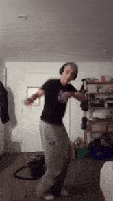 a man wearing headphones and a black shirt with a butterfly on it dancing in a room