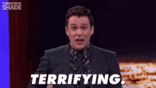a man in a suit and tie is saying terrifying while standing in front of a curtain .