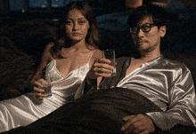 a man and a woman laying on a bed holding glasses