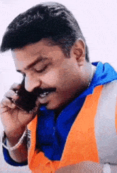 a man in an orange vest is talking on a cell phone .