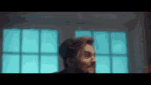 a man with a beard is standing in front of a window and looking out .