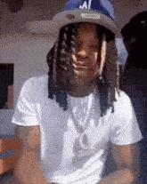 a man with dreadlocks and a hat is wearing a white shirt and a chain .