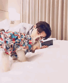 a man is laying on a bed with a dog wearing a shirt and looking at a cell phone .
