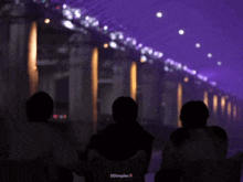 three people are standing in a dark room with purple lights behind them ..