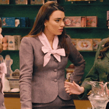 a woman in a gray jacket with a pink bow on her neck