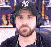 a man wearing headphones and a ny hat looks at the camera