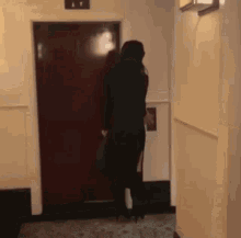 a woman in a black dress is standing in front of a red door in a hallway ..