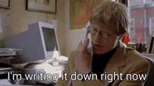 a man talking on a phone with the words i 'm writing it down right now