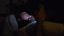 a man with a beard is laying in bed using a cell phone