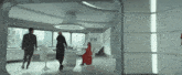 a woman in a red dress sits at a table in a room with people walking around it