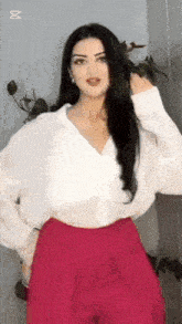 a woman wearing a white shirt and pink pants is standing in front of a wall .