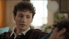 a man with curly hair is sitting on a couch looking at another man