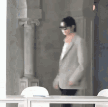 a man wearing a suit and glasses is walking in a room with white chairs .